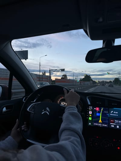The interior of a moving Citroen vehicle is captured during twilight, heading toward Selyatino, Russia. The driver, wearing a light-grey long-sleeved shirt, has both hands on the steering wheel. The speedometer reads 104 km/h. The navigation system displays a route toward the destination. The estimated time of arrival is 21:32, and the remaining travel time is 23 minutes. The route is indicated on the map, and the current location is 8 kilometers from the destination, which is along the Minskoye Highway. Exterior elements visible through the windshield include road signage, street lights, and the sky.