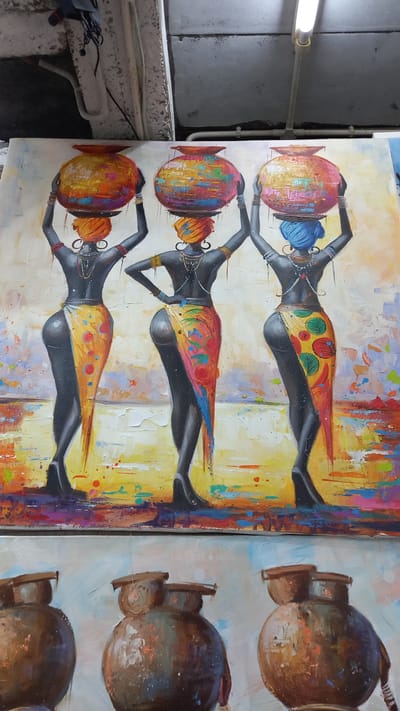 The image depicts two canvas paintings, likely displayed indoors. The left canvas features an artistic rendition of three African women in a row, balancing colorful jugs on their heads. They are depicted with dark skin, stylized clothing, and decorative head wraps. The background is a blend of vibrant colors. The right canvas shows a series of brown pots or urns. The location in Ban Ao Nang, Thailand is not ascertainable from the image alone.