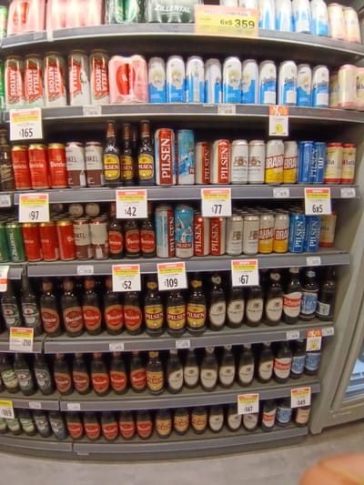 The image captures a well-stocked supermarket shelf filled with various brands and types of beer. The shelves are organized by beer brand and form factor (cans and bottles). Price tags accompany each selection. The beers featured include Stella Artois, Pilsen, Patricia, Nortena, Quilmes, Brahma, Heineken, and Schneider. The shelves are well-lit. The supermarket is likely located in Montevideo, Uruguay, given that these beer brands are commonly found there. The environment appears to be a typical retail setting, with a focus on product display. There are no people visible in the frame, and the objects are stationary.