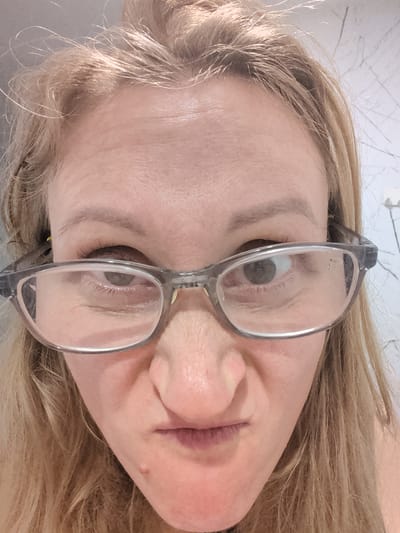 A close-up, rotated view of a blonde woman's face wearing glasses. The background is ambiguous. There is no evidence that this image was taken in Ko Pha-ngan, Thailand.