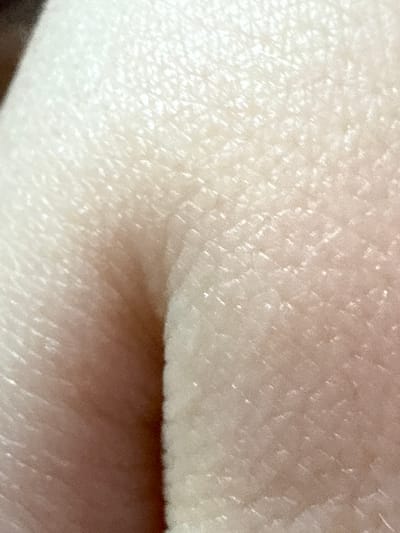 The image is an extreme close-up of human skin, likely from a finger or hand, showing the texture of pores and fine lines. The skin appears fair with a slight pinkish hue, illuminated by a soft light source that creates highlights and subtle shadows. The focus is very tight, rendering any larger context of a person, object, or setting indistinguishable. There are no discernible activities or events taking place, as the image is static and abstract. The lack of environmental cues means time of day, weather, or specific location within Ulan-Ude, Russia cannot be inferred. No text is visible in the image. The overall impression is one of microscopic detail and the natural surface of human skin.