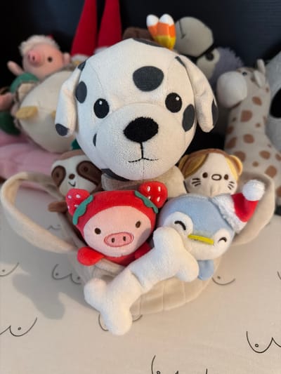 The image shows a collection of stuffed animals. Included are a Dalmatian, a giraffe, a gray stuffed animal, a pig with a strawberry design, a bird wearing a Santa hat holding a bone, a sloth, and a pig. A bag with a handle is also present. The photo was taken indoors. There is no indication that the photo was taken in Rueil-Malmaison, France.