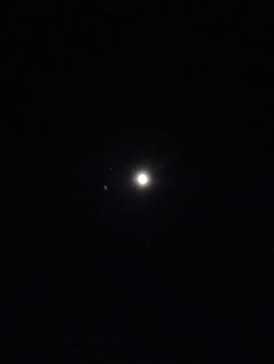 The image displays a nighttime sky with a prominent, bright moon. To the left of the moon, a smaller, faint object is visible. The background is entirely black, suggesting it is dark and likely devoid of significant light pollution, making the celestial bodies more visible. The image does not provide any visual information that would allow for identification of a specific location within Blanggurah, Indonesia, or any human presence.