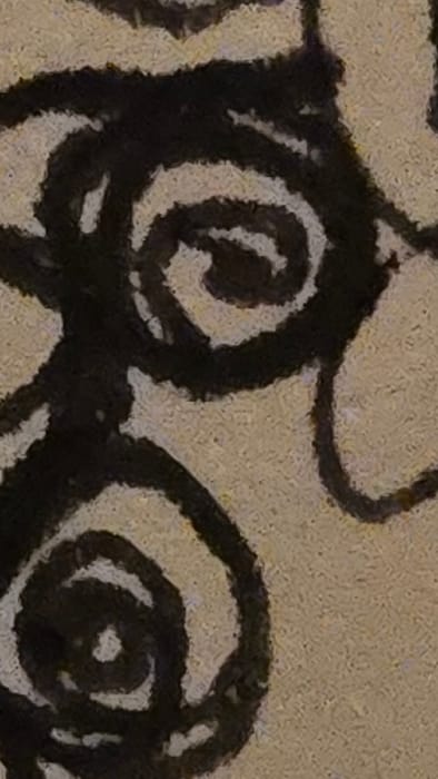 The image displays a highly magnified, abstract composition consisting of broad, dark, free-form curvilinear and spiral patterns overlaid on a lighter, textured, mottled beige and tan surface. Prominent features include two distinct, concentric spirals, one in the upper-center and another in the lower-left, connected and surrounded by several sweeping, dark lines that interlace across the frame. The background texture exhibits a granular or coarse appearance, possibly suggesting canvas or a rough wall. No human figures, identifiable objects, specific actions, or environmental context indicating a location within Lompoc, United States, are discernible.