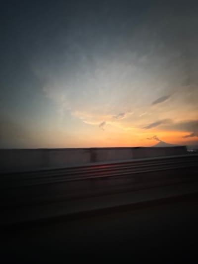 The image shows a view from inside a building, possibly a house, looking out a window towards a cloudy sky. The sky transitions from dark gray on the left to a brighter orange color towards the center and right, suggesting either sunrise or sunset. The window frame is visible on the right side of the image and is partially obscured by darkness, implying the room is dimly lit. The presence of a window implies the location is an interior space. Without further information, precise details about the location in Tlaxcalancingo, Mexico, are indeterminable. No people, actions, or interactions are visible.