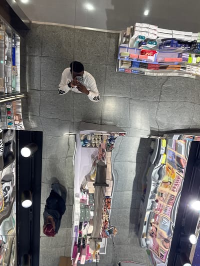 A person is taking a selfie in a store. The store has a polished, reflective floor that distorts the surroundings. There are shelves stocked with various products, possibly cosmetics or personal care items, visible in the reflection. The person is wearing a white long-sleeved shirt. The image is taken from a high angle, looking down. The location of Guta, China, is not evident from the image.