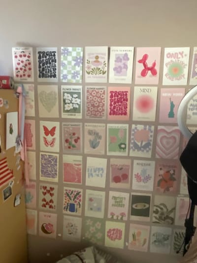 This media file shows a wall decorated with a grid of small, square prints. The prints feature various designs, including abstract art, floral patterns, illustrations of objects like balloon dogs and fruit, and text-based graphics. Some prints have text that is partially visible, such as "ONLY POSITIVE ENERGY," "MIND," "NEW YORK," "MATISSE," "FLOWER MARKET," "FRUIT MARKET," and "TREAT PEOPLE WITH KINDNESS."

The wall appears to be indoors, possibly in a bedroom or living space, given the artistic and decorative nature of the display. The lighting suggests it could be daytime, but there are no strong cues for time of day or weather. The overall aesthetic of the prints is whimsical and cheerful, with a color palette dominated by pastels and bright accents.

On a surface below the wall, a can and some other small items are visible, including what looks like a notebook and some striped paper. The focus of the image is the wall art. The setting is identified as Мухавецкі сельскі Савет, Belarus.