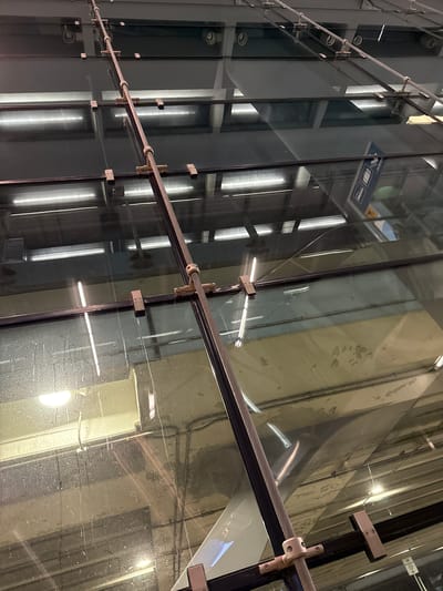 The image shows the architectural details of a modern building, characterized by its glass facade and visible structural elements. The building's exterior is made up of a series of large glass panels, supported by a network of metal rods and connectors. The reflections in the glass reveal the interior spaces, including what appear to be elevator shafts and interior lighting. The overall appearance is industrial and contemporary, suggesting a commercial or institutional space. It is located in the city of Chicago, United States.