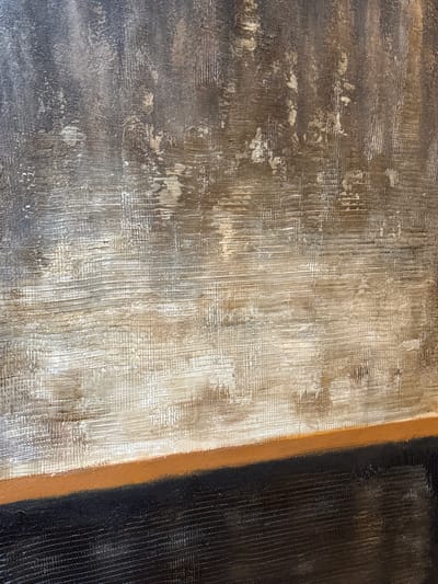 The image presents a close-up, abstract view of a highly textured surface, likely a painting or a decorative wall panel. The composition is divided into three distinct vertical sections, primarily defined by color and texture.
The leftmost section features a mottled blend of dark grey and brown tones, with irregular lighter, almost metallic-gold or beige patches and streaks. This area exhibits a rough texture, showing both horizontal and vertical marks.
Adjacent to this, the central section is predominantly lighter, characterized by shades of off-white and light beige. It displays a pronounced, finely detailed texture composed of numerous vertical lines and subtle cross-hatching, giving the impression of a woven fabric or deeply brushed paint. Warm, light brown undertones are present within this lighter area.
A thin, distinct vertical stripe of earthy orange-brown color acts as a boundary, separating the central section from the rightmost portion of the image. The right section is a solid, dark, almost black color, also featuring a vertical textured pattern consistent with the brushed or linear style seen in the central section.
No specific objects, people, or activities are depicted. The focus is entirely on the interplay of color, texture, and light across the surface. There is no visible text, and no external cues indicating time of day, weather, or a specific location within the image itself.