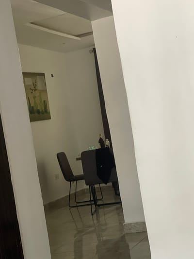 The image appears to be taken from a high vantage point, possibly through a doorway or window. The view looks into a room with white walls and tiled floors. A gray office chair is visible near a dark table or desk. A picture hangs on the wall. The room seems to be in a residential or office space. The location in Iddo Tudunwada, Nigeria cannot be confirmed from this image. No people are visible.