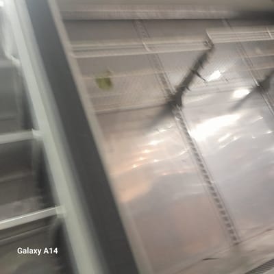 The image appears to be taken inside a room or enclosed space, possibly a building interior, in Nuseirat, Palestinian Territory. The focus is on the ceiling or upper portion of a structure featuring metallic grating or mesh-like panels. Light is reflecting off the surfaces, creating glare and obscuring finer details. A vertical structural element, possibly a pillar or wall, is visible on the right side of the frame. There is a greenish object or spot on the right side of the frame, but it is unclear what it is. The overall image quality is poor, with motion blur, making it difficult to ascertain more specific details.