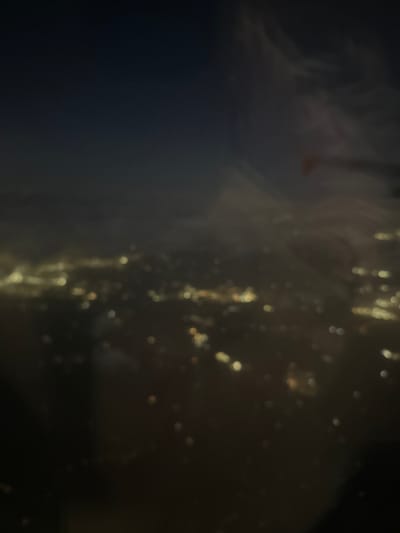 The image shows an out-of-focus view of what appears to be city lights at night. The left side of the frame is dominated by darkness, while the right side contains blurred, yellowish lights, possibly from streetlights or buildings. Given the location of Tremblay-en-France, it could potentially depict an aerial view of city lights from a high vantage point. However, the lack of focus makes it difficult to discern specific details.