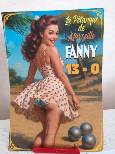 The image shows a vintage-style poster featuring a woman in a polka-dot dress, seemingly in a playful pose. She has red hair styled in curls and is smiling at the viewer. The poster has text that reads "La Pétanque de Marseille" and "FANNY 13-0". The background depicts a sunny outdoor scene with palm trees and a grassy area, suggesting a vacation or beach setting. In the foreground, there are three boules, one smaller than the others, used in the game of pétanque. A red object, possibly a game piece or a part of the poster's frame, is visible at the bottom. The poster appears to be slightly worn, with some creases and signs of age. The city of Oliveira do Bairro, Portugal is not depicted in this image.