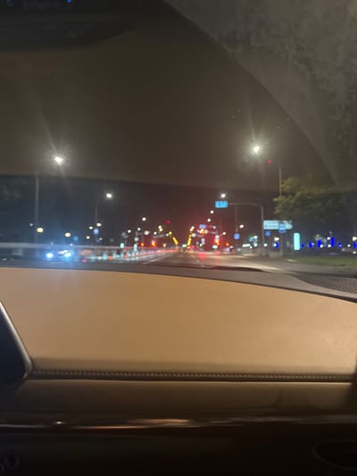 The image depicts a view from inside a vehicle at night, looking through the windshield at a city street. The scene is characterized by a low level of ambient light, with numerous streetlights and vehicle headlights illuminating the surroundings. The road ahead appears to be a multi-lane thoroughfare with traffic lights and various signs visible. The interior of the vehicle is partially visible, with a light-colored dashboard in the foreground. The overall impression is one of urban nighttime travel. The reference to Vnukovo, Russia, suggests a possible geographical context for the scene.