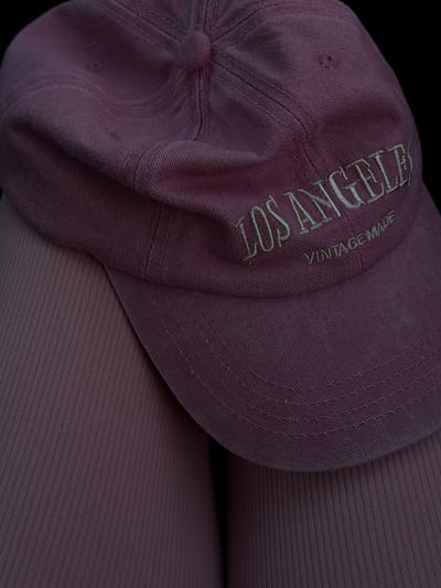 A close-up shot shows a pink baseball cap with the embroidered text "LOS ANGELES" and "VINTAGE MADE" on the side. The cap is resting on what appears to be ribbed fabric of a similar pink hue, possibly clothing. The background is entirely black. There are no discernible elements that indicate a location in Gorzow, Poland.