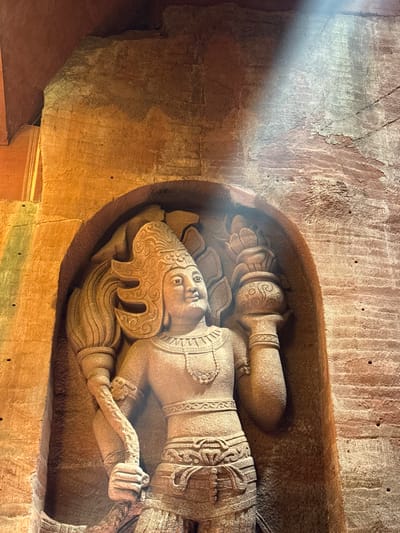 The image shows a stone carving of a reclining figure, possibly a deity or important person, recessed into a wall. The figure is detailed, with decorative clothing, elaborate headdress, and an object held in one hand. The stone wall appears aged and textured. A beam of light falls on the carving, highlighting the features. This image is from the city of Shizhong, China.