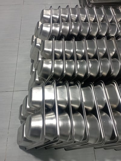 The image shows stacks of metal food trays. Each tray has two compartments, one square and one round. The stacks are likely stored in a kitchen or food service area. The image does not show any people or specific actions. The background is a tiled wall. No specific location details within Dayahtuha, Indonesia, are discernible from the image.