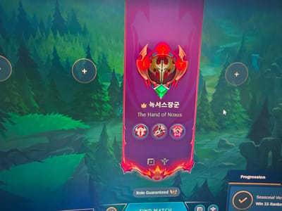 The image shows a computer screen displaying a League of Legends game interface. A vertical banner with a red and gold emblem at the top dominates the center of the screen. The emblem features a green gem in the middle. Below the emblem are Korean text and the English translation, "The Hand of Noxus." Three circular icons are arranged below the text. Further down, there is a "Role Guaranteed" tag and icons. At the bottom, the words "FIND MATCH" are partially visible.
To the right of the banner, a section titled "Progression" is visible, with a checkmark and the text "Seasonal Victories - Win 15 Ranked Games." The background of the screen depicts a forest scene with trees. There are circular icons with plus signs in the background as well.