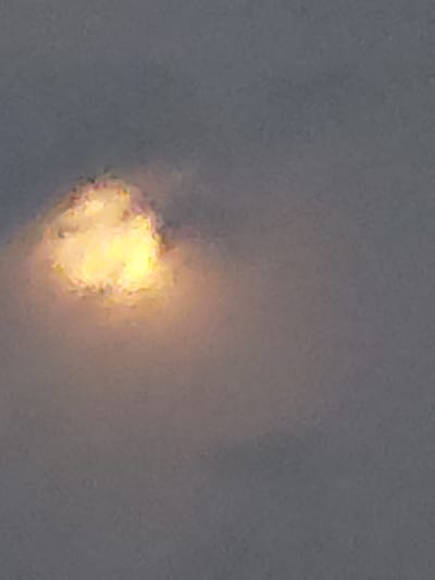 The image shows a close-up, somewhat blurry view of a bright, yellow, and orange light source against a muted gray background. The light source appears to be surrounded by wisps of lighter color, possibly smoke or clouds. The texture of the light source is irregular, with brighter, more intense areas and softer edges. The overall impression is of an intense, localized light. Given the context of Kyzylorda, Kazakhstan, this could potentially be a flare, a distant explosion, or a bright celestial object obscured by atmospheric conditions. The time of day and weather are not definitively discernible, though the soft lighting might suggest dawn or dusk, or perhaps an overcast sky. There is no visible text in the image.