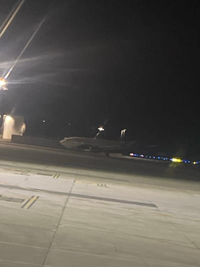 At night in Močići, Croatia, a partial view from above shows what appears to be an airport runway or tarmac. The surface is marked with lines and striping. A vertical line of lights is visible to the side of the runway. Streetlights provide illumination in the lower part of the frame.