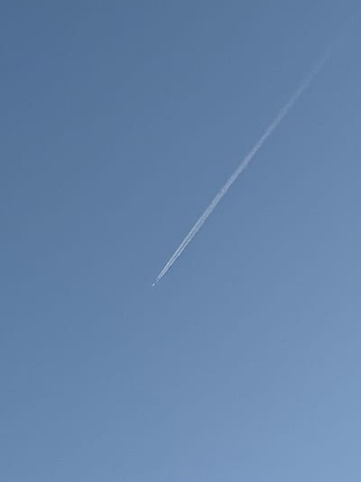 The image shows a clear blue sky with a contrail from an airplane. The contrail is a long, thin white line that extends diagonally from the upper right to the lower left of the frame. There is a small, indistinct object at the bottom of the contrail, which is likely the airplane itself. The scene is devoid of any landmarks or identifying features that would allow for localization to Dusseldorf, Germany.