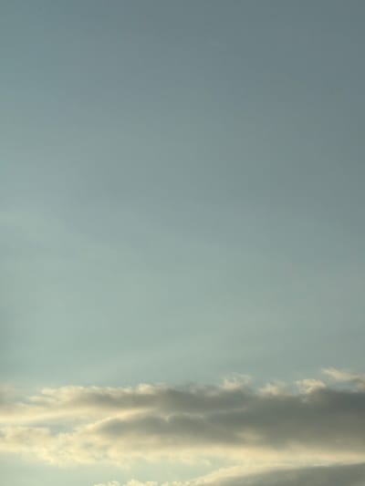 The image shows a clear sky with scattered clouds. The sky is a pale blue, and the clouds are white and gray. There are no people or objects visible in the image. The scene is peaceful and serene.