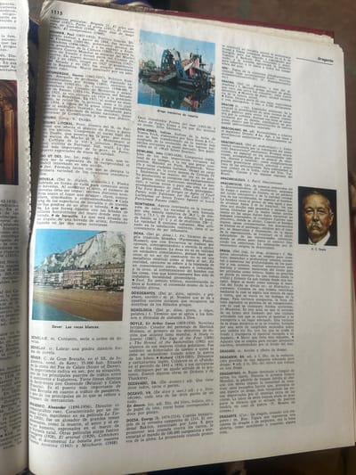 This media file is a scan of a book's open pages, displaying text and images. One page features a portrait of a man, identified by visible text as "A. C. Doyle." The surrounding text includes entries for various words and names, such as "dragante," "Dover. Las rocas blancas," and biographical information. The other page is filled with dense text and two images: one is a close-up of a large ship or industrial equipment, possibly a crane or a part of a dockyard; the second image is a wide shot of a coastal town with buildings lining the shore and a prominent rock formation in the background. The overall impression is that of an encyclopedia or dictionary, with the images serving as illustrations for the entries. The text is in Spanish, and the content appears to be informational, likely pertaining to history, geography, or biographical entries. The lighting suggests an indoor setting, possibly a library or study, with the book laid flat on a surface. There are no overt indications of time of day or weather, but the overall scene is static and informative.