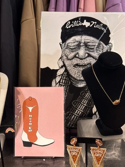 A collage of objects presents a collection of items. A portrait of Willie Nelson is prominently displayed, alongside a black jewelry display showcasing a delicate gold necklace. Earrings hang nearby, with a football theme, including fringe with "Game Day." A pink card depicts a cowboy boot with a Longhorns logo. Clothing items can also be seen in the background.