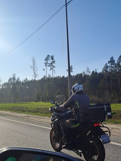 The image shows a motorcycle on a road with a rider wearing a white helmet. The license plate on the motorcycle reads "6693 BO 50 RUSS." The surrounding environment includes trees, grass, and a clear blue sky with power lines. The location is Pokrov, Russia.