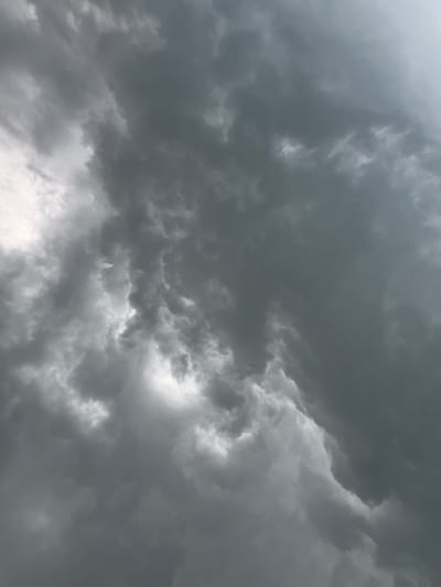 The image is a close-up, low-angle shot of dark, dramatic storm clouds filling the sky. The clouds are dense and turbulent, with swirling formations and varying shades of gray. Patches of brighter light are visible through breaks in the clouds, suggesting the presence of the sun behind them. The overall impression is one of an approaching storm. There are no visible buildings, people, or any other discernable elements of a cityscape. The location of Маяк, Russia is not evident from the image itself.