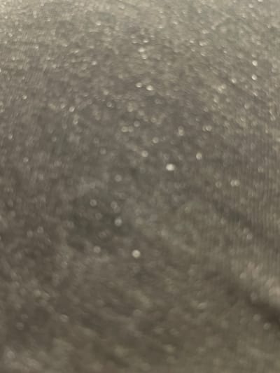 The image is an out-of-focus, close-up shot of a textured, gray surface with numerous small, bright highlights. The highlights appear as bokeh, suggesting they are out-of-focus points of light reflecting off the surface. The texture of the surface is granular and somewhat uneven, with subtle variations in tone. There are no discernible objects, people, or actions present. The background is uniformly gray and lacks any distinct features. There is no information in the image that would allow for its location to be determined, including in Kołobrzeg, Poland.