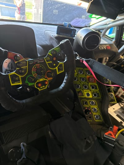 The image depicts the interior of a Huracan GT3 EVO2 race car. Focus is on the steering wheel, which features various controls labeled "START," "SPEED-LIMITER," "DRINK," "BOX KILL," "RADIO," "GRIP," "FLASH," and "TC GRIP/LAT." The steering wheel also displays a numbered dial labeled "MIX." A dashboard with multiple yellow-bordered buttons is visible above the steering wheel. Harness straps are also evident. In the background is the GT3 Logo. The location of Campagnano di Roma, Italy is not discernible from this image.