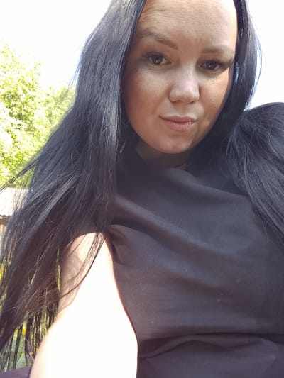A woman with long, dark hair is taking a selfie outdoors. She is wearing a black shirt. Part of a tree is visible in the background. It is daytime. There is no evidence to suggest this photo was taken in Кипчак, Russia.