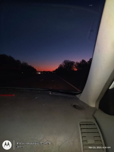 A dim, tilted photograph captures a car's interior against a sunset backdrop. Visible are the vehicle's dashboard, including vents and trim, alongside a window displaying a twilight sky. The horizon features a fading gradient of orange and blue. The image's date stamp reads "Nov 26, 2025, 6:36 AM," and camera information is overlaid: "shot on moto g stylus 56-2024 Dock-ši".