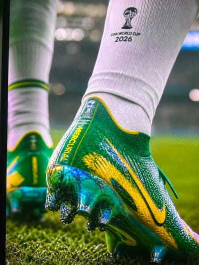This media file features a close-up shot of a person's leg wearing a white soccer sock and a green and yellow soccer cleat. The cleat has a distinctive iridescent finish, with shades of blue and green reflecting on its surface. The shoe prominently displays the "MERCURIAL" branding in yellow text.

On the sock, the "FIFA WORLD CUP 2026" logo is visible, indicating a connection to the upcoming FIFA World Cup. The background consists of a blurred green grassy field, suggesting a soccer or sports setting. The lighting is bright, and there are no explicit indicators of time of day or weather conditions. The focus is on the sports equipment, highlighting the details of the cleat and sock.

The image is cropped and appears to be a screen capture, possibly from a video game or promotional material. The overall impression is one of sport and athletic performance, with a clear emphasis on the FIFA World Cup branding. The location context provided is Cadek, Indonesia, which may be relevant to the specific team or player represented by the cleat's design.