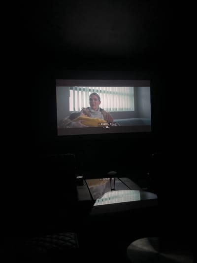 A screen displays a scene with a person in front of blinds, with subtitles that read "- Claro, sí. - Sí.". The scene is dark, and the screen is positioned to the right of another screen or surface. The location is in Zibatá, Mexico.