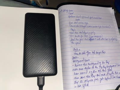 The image presents an overhead view of a black portable hard drive and an open notebook, positioned on a light-colored surface within an indoor setting in Hayin Banki, Nigeria. The hard drive, featuring a distinct diagonal striped pattern, is connected via a black USB cable and occupies the left side of the frame.
To the right, the notebook displays extensive handwritten notes in blue ink on lined paper. The text details instructions and concepts related to video editing, with visible headings such as "Capcut editing Tours" and "Skills." Specific notes refer to "Epidemic Sound - of a sound effect, Jouch/BGM," and various editing techniques like "Chimentals overlays & seake & Transction & gfa & Turbulent."
Further down, "Step 1" outlines foundational editing processes: "Add clips and adjust propely," "pick turator for Lips (ince remappery)," and "fund the beat and fost it with the Clop. by adjusting the speed." A section labeled "Skill 2" delves into "How to add Glow and design lys," listing "Tools - Background esser." Detailed instructions include "Remove the background of the hip," applying "touches to the Cup by background has been moved e.g Blur 5% and glow," and using methods such as "mask of with the V Clip su only one pat gets applied Cow chane" and "Use splice."
The scene suggests an individual engaged in planning or learning about video production, using an external storage device for digital assets and taking meticulous notes. The lighting is consistent with an indoor environment, offering no specific cues about the time of day. A dark, possibly textile, surface is partially visible at the top left corner, hinting at a casual workspace.