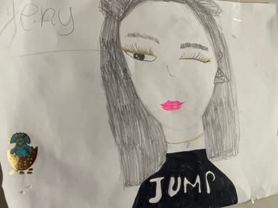 This is a photograph of a child's drawing on white paper. The drawing depicts a stylized portrait of a person with dark hair, yellow eyeliner, and bright pink lips. The person is wearing a black shirt with the word "JUMP" written on it in white letters, and a gold necklace with a cross pendant. To the left of the drawing, there is a small, gold-colored sticker of a blue dinosaur hatching from an egg. The word "Jeny" is written in faint pencil at the top left of the paper. The overall impression is that of a creative piece by a child. There is no discernible location in the city of Cahul, Moldova, associated with this image.