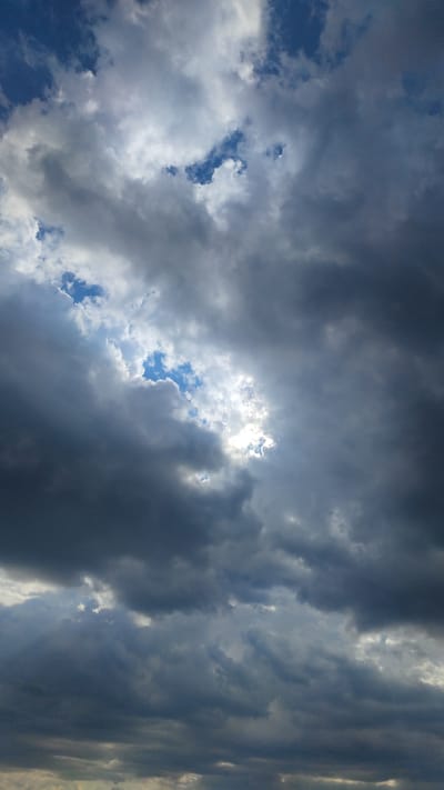A vertical, low-angle shot captures a dramatic sky filled with dense, dark storm clouds. Patches of bright blue sky are visible through openings in the clouds, with sunlight piercing through in some areas, creating a sense of depth and contrast. The clouds exhibit varying textures and shades of gray, from light and wispy to heavy and ominous. The overall impression is one of an impending storm or the aftermath of one. There are no visible people, subjects, objects, or actions in this image, and the location in Pitkyaranta, Russia, is inferred and not visually evident.