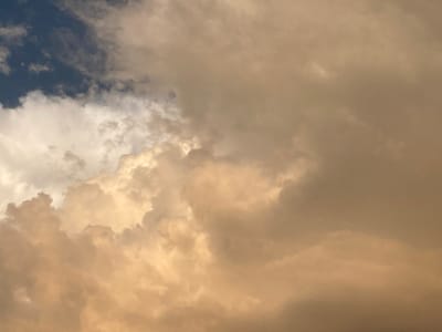This media file depicts a dramatic sky filled with large, billowing clouds. The clouds are predominantly in shades of gold and brown, suggesting either a sunset or sunrise, or perhaps a stormy weather condition. In the upper left corner, a patch of deep blue sky is visible, contrasting with the warmer tones of the clouds. There are no people, objects, or discernible structures within the frame; the focus is entirely on the atmospheric phenomenon. The image captures a sense of grandeur and power in nature, with the textured and layered clouds creating a dynamic and somewhat ominous visual. The overall impression is one of a vast and awe-inspiring sky, likely in a rural or open setting given the lack of urban elements. There is no visible text in the image.