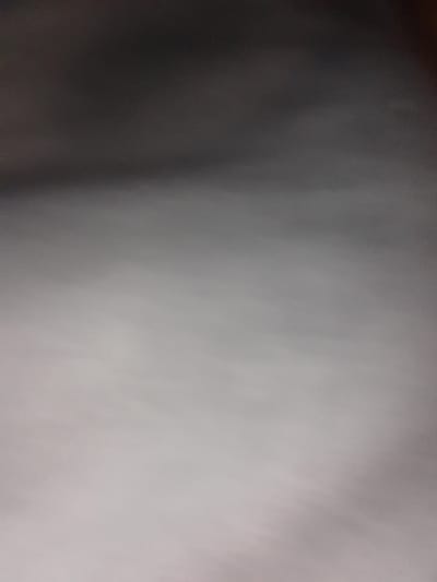 This image is a close-up, slightly blurred photograph of a textured, monochromatic surface. The dominant colors are shades of gray, transitioning from dark gray at the top to lighter shades of gray and off-white towards the bottom. There are no discernible objects, people, or actions visible in the image. The background appears to be a uniform, out-of-focus material. The location in Liubakhy, Ukraine, is not evident from the visual content of the image.