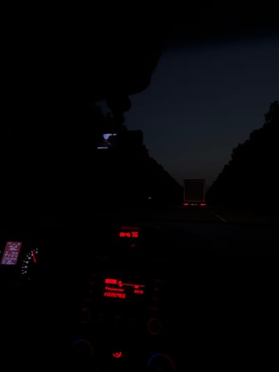 The image depicts the interior of a car at dusk or night, with the dashboard lights illuminated. The view is from the driver's perspective, looking out through the windshield onto a road with a semi-trailer truck in the distance. The dashboard shows a digital display with information such as "489 km", "72 l/100", and "D 206815". There is also a tachometer visible. A red digital clock on the dashboard displays "20:45 23:". The background outside the car shows a dark sky with trees lining the road and the illuminated rear of the semi-trailer truck. The location of Anatol'evka, Russia is not visually discernible from the image content.
