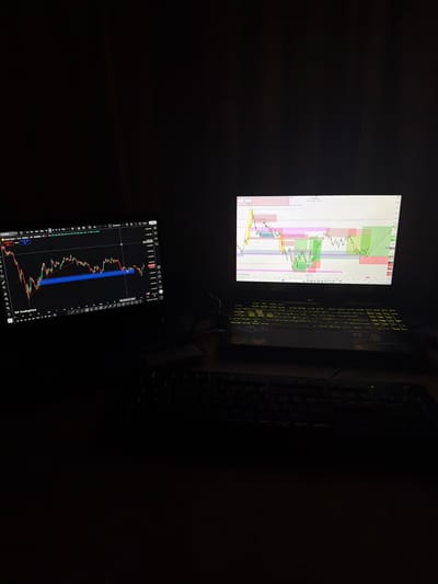 Here is a detailed description of the image:
**Scene:** The image depicts a dimly lit indoor environment, likely a home or office workspace.
**Objects:**
* **Two screens:** One appears to be a computer monitor displaying a financial chart, and the other is a tablet also displaying a similar chart.
* **Keyboard:** A black keyboard with illuminated keys is visible to the right of the monitor. The keys appear to have a yellowish illumination.
* **Financial Charts:** Both screens display what appear to be financial charts, likely related to stock or currency trading.
* **Dark Environment:** The background and surrounding areas are mostly dark, suggesting low ambient light.
**Details:**
* The financial charts seem to display candlestick patterns, which are common in financial analysis.
* The tablet is labeled "TradingView", indicating a likely platform used for financial analysis.
**Location:**
* There is no information in the image to provide a location of the city Ede, Netherlands.