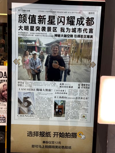 Here is a description of the image provided:
**Scene:** A person is standing in front of a screen that displays a souvenir newspaper-like image of themselves, taken at a tourist spot likely in Chenghua District, China.
**Newspaper Details:** The image shown on the screen mimics a newspaper front page with Chinese text and images. The headline features the phrase "A New Star Lights up Chengdu". The paper includes the person's photo within a mock news story and various other articles (in Chinese) related to Chengdu's attractions, food, and culture. There are arrows on the paper indicating ways to slide the images.
**People:** In the photo within the newspaper are several people, presumably the person and their companions. They are casually dressed and appear to be tourists.
**Objects:** The screen on which the newspaper souvenir is displayed, features a "Begin to Photograph" button, the price for printing the newspaper is displayed.
**Environment:** The scene is indoors, possibly in a souvenir shop or photo booth area, with modern design. The background is dimly lit compared to the screen's brightness.