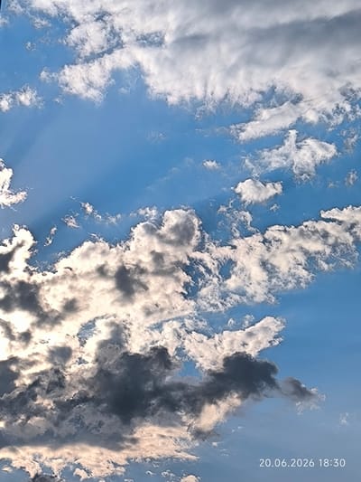 The image is a close-up, high-angle shot of a blue sky filled with a mixture of dark and light clouds. The clouds are textured and appear to be in motion, with some showing bright sunlight peeking through. In the bottom right corner of the image, a date and time stamp reads "20.06.2026 18:30". There are no people, animals, or man-made structures visible in the frame. The scene appears to be an outdoor environmental shot, likely taken in Surgut, Russia, given the date format and common timestamping practices.