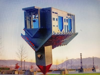 The image depicts an upside-down sculpture resembling a building with blue windows and red accents, mounted on a tall, slender support structure. The sculpture is situated outdoors in what appears to be a park or public space. In the background, there are bare trees, distant mountains, and two lampposts. The sky is overcast and shows a gradient of light colors, suggesting either dawn or dusk. There are a few indistinct figures visible in the distance near the lampposts. The foreground shows a pathway and some benches. The specific location in the city of Sluck, Belarus is not identifiable from the visual information provided.