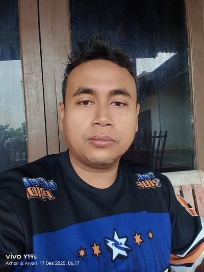 A medium shot captures a man with short, dark hair. He wears a black and blue shirt adorned with star-shaped designs. The "COOL RIDE" logo is visible on the shirt. He stands near a window, reflecting an outdoor scene. A watermark on the lower left reads "vivo Y19s Akhtar & Arvan 17 Des 2025, 06.17". The background is partly wooden with a building visible through the window.