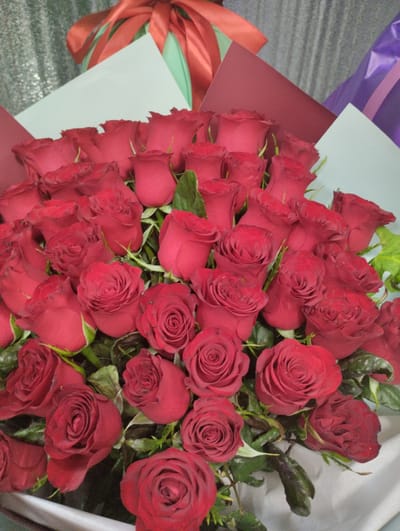 This media file displays a close-up view of a large bouquet of red roses, likely a gift or decoration. The roses are varied in their bloom, with some tightly budded and others fully opened, revealing intricate petal formations. Their deep red color is rich and vibrant. Scattered green leaves and stems are visible amongst the blossoms, adding a natural contrast.
The bouquet is partially wrapped in layers of decorative paper. The outer layers include a deep red paper, and a lighter pastel paper, possibly pale blue or mint green. Behind these, elements of a red ribbon are visible, suggesting the bouquet is tied with a bow. In the background, hints of other wrapping materials can be seen, including what appears to be a purple and possibly a pink textured paper, suggesting a more elaborate presentation. The overall presentation implies a special occasion, such as an anniversary, Valentine's Day, or a romantic gesture.
The lighting suggests an indoor setting, possibly a room with artificial light, as there are no clear indicators of natural daylight or weather conditions. The focus is entirely on the roses, emphasizing their beauty and abundance. There is no visible text within the image. The setting appears to be Kostanay, Kazakhstan, though this information is contextual and not visually evident in the image itself. The emotions conveyed are those of romance, passion, and appreciation, commonly associated with red roses.