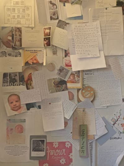 This image shows a collage of papers, photos, and cards pinned to a wall. The content appears to be personal, featuring baby photos, handwritten notes, and decorative cards. The items are arranged haphazardly, creating a dense and cluttered visual effect. Some of the papers have French text, referencing Tourcoing, France, and names such as Auguste Bailleve, Gatien, and Louis. The image depicts an intimate and sentimental collection of memories.