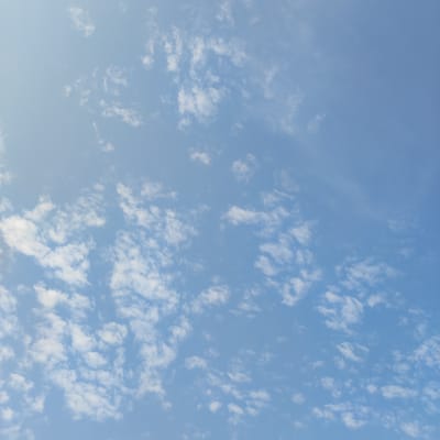 The image shows a clear blue sky with scattered white clouds. The clouds are thin and wispy, with some appearing to be in small clusters. The lighting suggests it is daytime. There are no people, subjects, objects, actions, or interactions visible. The environment is solely the sky. This scene could be observed from any outdoor location, including Krutinka, Russia.